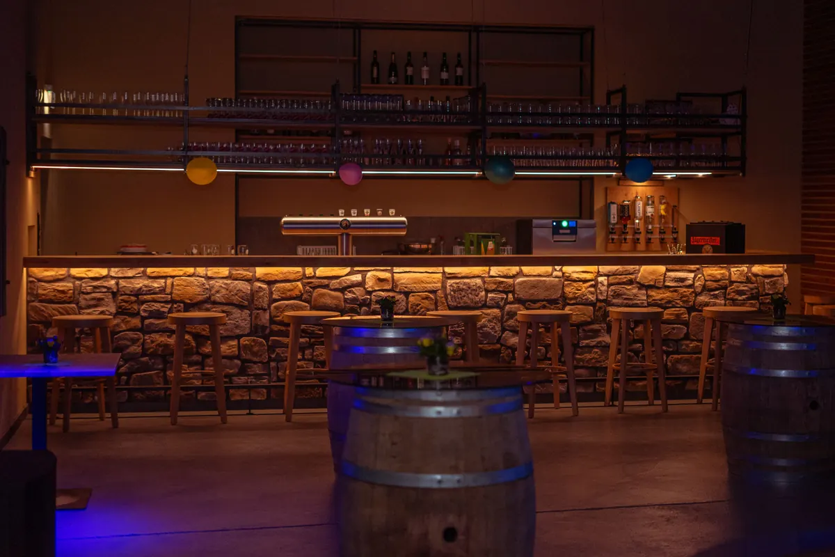 Bar am Abend mit beleuchteter Natursteintheke, Fasstischen und farbigen Lichtkugeln
