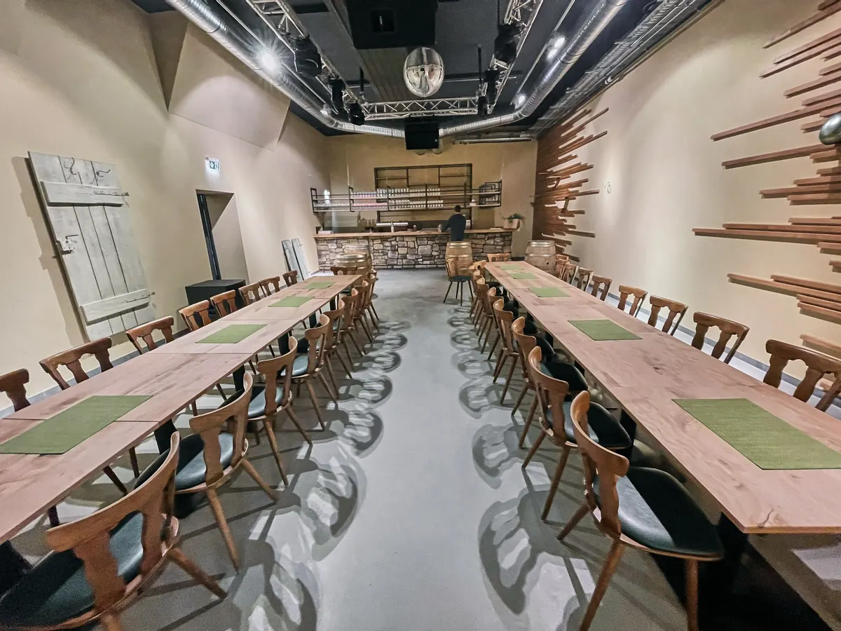 Großer Saal mit zwei langen Tafeln, Natursteintheke und Holzlattenwand